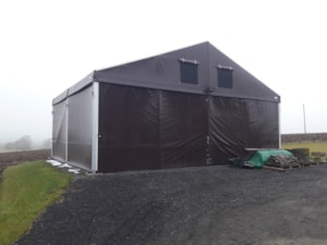 Agricultural tent hall with dark cladding and ventilation windows in the gable