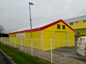 Stanová hala se žlutým opláštěním a červeným lemem – u oplocení